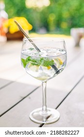 Gin And Tonic In A Glass With Fresh Mint, Slices Of Lemon And Ice Cubes In A Garden On A Sunny Day