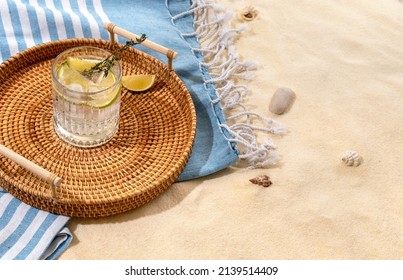 Gin tonic with lime on a wicker tray on beach with white sand. Summer sea vacation and travel concept. Exotic summer drinks. 