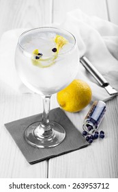 Gin and tonic on a highball glass with a lemon twist and juniper berries