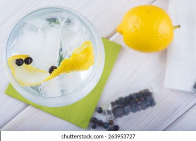 Gin And Tonic On A Highball Glass With A Lemon Twist And Juniper Berries