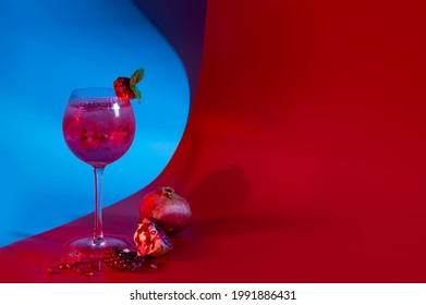 Gin And Tonic Pomegranate Cocktail With Ice Cubes And Mint Leaves On Abstract Red And Blue Background. Neutral Copy Space