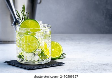 Gin tonic with rosemary cocktail drink with dry gin, bitter tonic, lime and ice. Gray background 