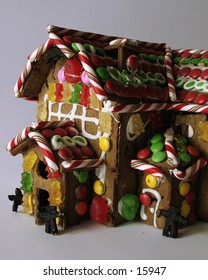 A ginger bread house seen from the front with little people standing in the doorway.