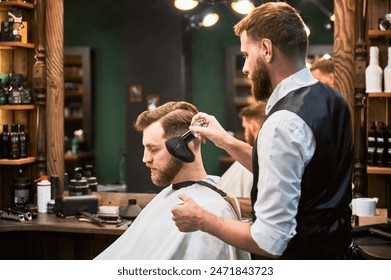 Ginger brutal man getting trendy haircut while sitting in white cape. Professional hairdresser using soft brush to sweep away the rest of cut hair. Final touches on fresh haircut. - Powered by Shutterstock