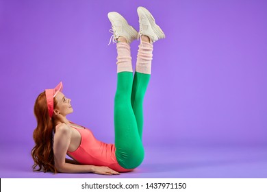 ginger girl makes warm up exercises before her fitness training, raises both legs up, hands on floor, looks with smile on her new white training shoes that bought recently aerobics and fit workout - Shutterstock ID 1437971150