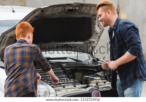 ginger\
hair father and son repairing car with open\
hood