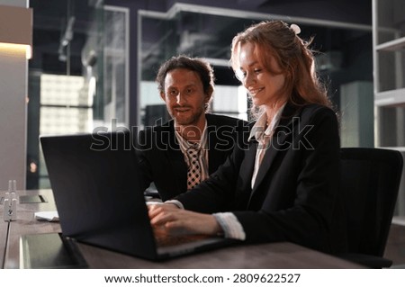 Ginger haired professional edits the file as her colleague follows each keystroke, lamp light soft on the desk between them in a bright modern coworking office during a collaborative.