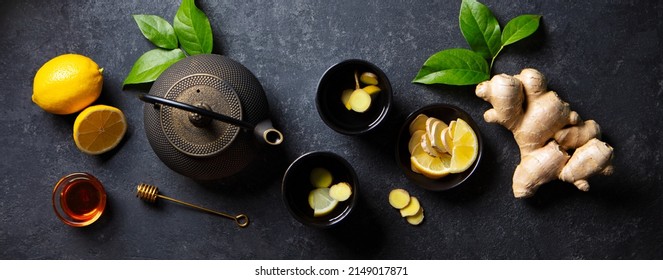 Ginger, lemon, honey tea in black cups , tea pot with fresh slices, roots. Dark background. Top view.