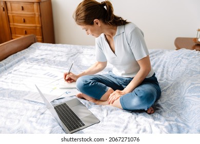 Ginger Mature Woman Writing Down Notes While Working With Laptop On Bed At Home