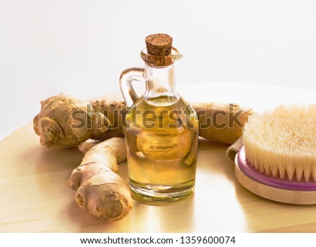 Ginger oil with fresh ginger roots and dry brush on wooden table. Therapeutic bath routine concept.
