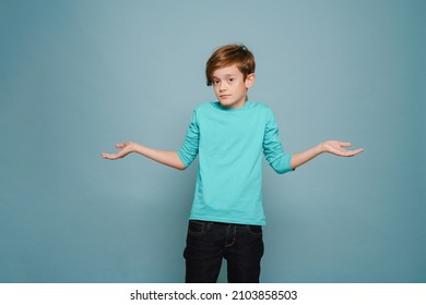 Ginger perplexed boy gesturing and looking at camera isolated over blue wall - Shutterstock ID 2103858503