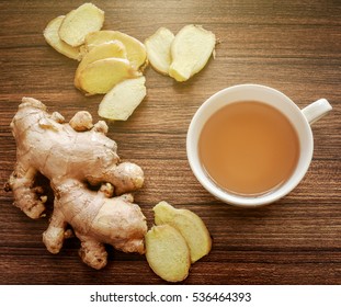 Ginger root and slices on wood background with a cup of ginger tea. Ginger tea helps warming the body in cold season, healthy drink. Soft light effect added.