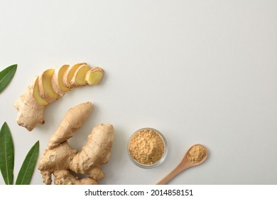 Ginger Root And With Slices And Powder In Glass Jar And Wooden Spoon On White Table With Leaves. Top View.