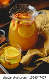 Ginger, Turmeric And Citrus (oranges And Lemon) Infused Hot Water With Goji Berries And Natural Honey In A Big Glass, Transparent Glass. Set On A Wooden Board With Decoration Of Dark Yellow Cloth. 