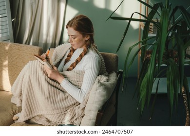 Ginger woman writing ideas in notebook, doing beauty face mask for skincare sitting in living room at home. Creative female looking thoughtful while planning - Powered by Shutterstock