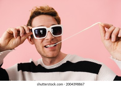 Ginger Young Man Wearing Sunglasses Stretching Bubblegum Isolated Over Pink Wall