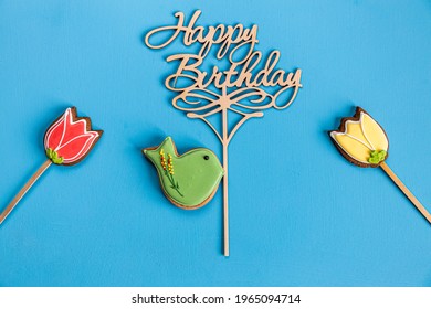 Gingerbread Bird Holding A Happy Birthday Sign And Two Flowers On Blue Background