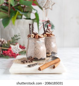 Gingerbread christmas chia pudding topped with hazelnuts and almonds in chocolate. Fit and healthy  vegan home-made dessert. Served in small jars on a marble board, with white background.  Front angle - Powered by Shutterstock