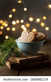 Gingerbread cookies in heart shapes decorated with icing in a blue bowl with Christmas lights bokeh and Christmas tree