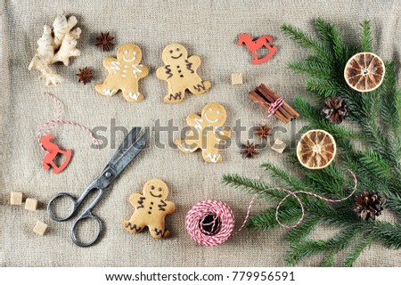 
Gingerbread in the form of little men on a canvas background. The Christmas composition is supplemented with the root of ginger, anise, cinnamon. In the frame scissors and thread. View from above.