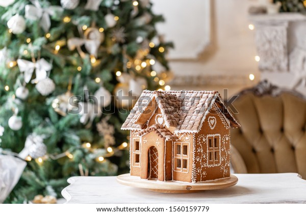 Gingerbread house, concept holiday of\
Christmas and Happy new year. Defocused lights of Christmas tree.\
Morning in the bright living room. Holiday\
mood.