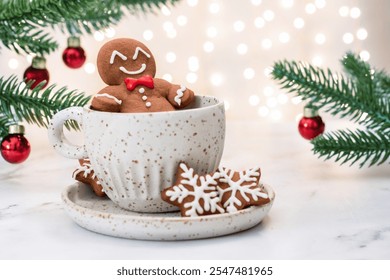 A gingerbread man is sitting in a cup of hot chocolate. The cup is on a white plate with a snowflake design. There are also several red and white Christmas ornaments in the background - Powered by Shutterstock