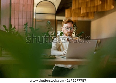 Ginger-haired man working on computer at cafe during lunch