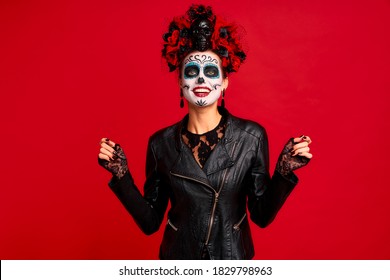 Gir with sugar skull makeup with a wreath of flowers on her head and skull, wearth lace gloves and dances during halloween party isolated on red background.Concept of Halloween or La Calavera Catrina.