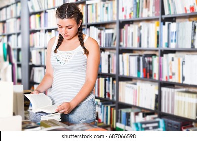 Girl 18-23 Years Old Is Choosing Interesting Book In Bookstore. 