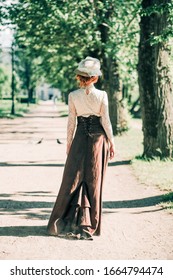 A Girl In A 19th Century Dress Walks In The Park