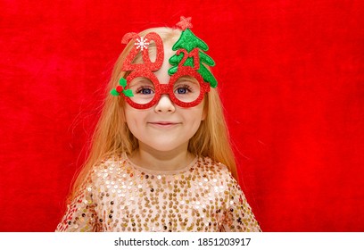 Girl 4 Years Old Blonde With Long Loose Hair Wearing New Year's Glasses With The Numbers 2021 Close Up On A Red Background