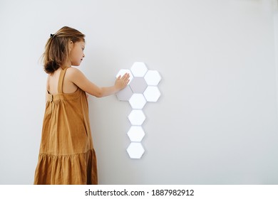 Girl Of 6 In Sundress Turns On Wall Touch Lamp. Luminaire Segments Folded In A Flower Shape