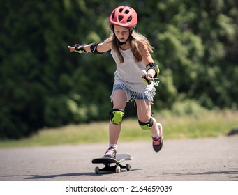 Girl (8 Year Old) With Helmet And Protection Gear Skate Boarding Outside In The Park In The Summer. Child On Skate Board.