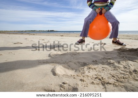 Girl (8-10) playing on inflatable hopper on beach, low section