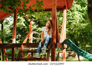 Girl 9 Years Old Cheerfully Sits Grimacing On A Wooden Playground Lifestyle Blond Long Hair Contagious Laughter Model Childhood Holidays Summer