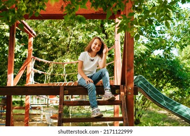 Girl 9 Years Old Cheerfully Sits Grimacing On A Wooden Playground Lifestyle Blond Long Hair Contagious Laughter Model Childhood Holidays Summer