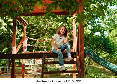 Girl 9 Years Old Cheerfully Sits Grimacing On A Wooden Playground Lifestyle Blond Long Hair Contagious Laughter Model Childhood Holidays Summer