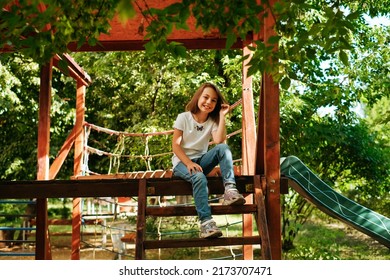 Girl 9 Years Old Cheerfully Sits Grimacing On A Wooden Playground Lifestyle Blond Long Hair Contagious Laughter Model Childhood Holidays Summer