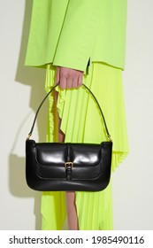 Girl In Acid Green Jacket And Pleated Skirt With Luxury Black Leather Handbag In Her Hand. Vertical Fashion Photo. Side View.