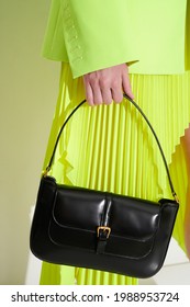 Girl In Acid Green Jacket And Pleated Skirt With Luxury Black Leather Handbag In Her Hand. Vertical Fashion Photo. Closeup.