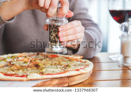 Girl adding spices on top of pizza with Mozzarella cheese, Tomatoes, pepper, olive, Spices and Fresh Basil. Italian pizza. Pizza Margherita or Margarita on wooden table background