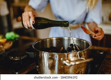 Стоковая фотография: Girl adding white wine to a pan with mussels, woman preparing food