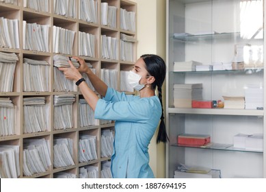 The girl administrator of the medical clinic finds the necessary patient card in the drawer of the rack and checks the correspondence of the last name. - Powered by Shutterstock