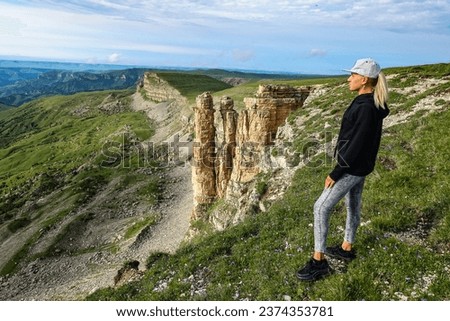 A girl against the background of two monks rocks in a cloud, Bermamyt plateau, Russia 2021.
