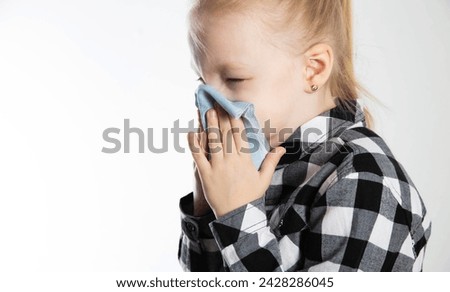 A girl aged seven years old in a checkered shirt blows her nose into a handkerchief on a white background. The concept of nasal congestion due to allergies and acute respiratory infections. 