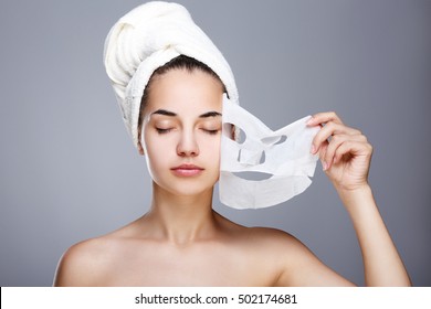 Girl with almost rended white mask. Model pulling away mask from her face. Closed eyes. Head and shoulders, studio, indoors