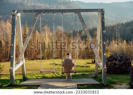 the girl alone on the background of nature;
the girl sits on a swing with her back to the camera and looks at the mountain landscape