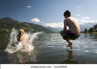 girl already in the splashing water and boy in the air while they where jumoing into a lake, with nice nature and mountains in the back - Powered by Shutterstock