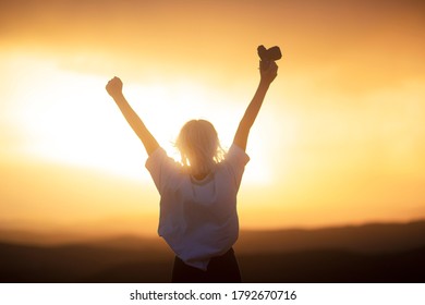A girl in a amazing sunset with her arms wide open and a camera in her hand. - Shutterstock ID 1792670716