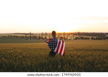 Girl with the American flag in a barley field at sunset. Independence Day, Patriotic holiday. 4th of July.  